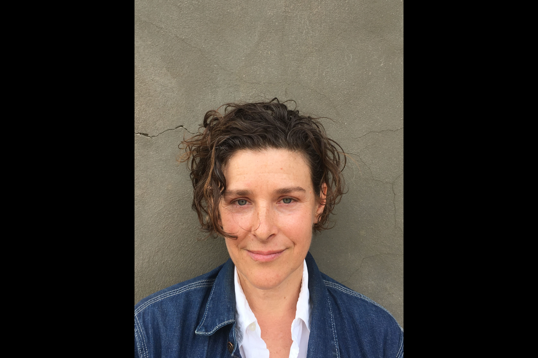 A woman smiling in front of a grey wall